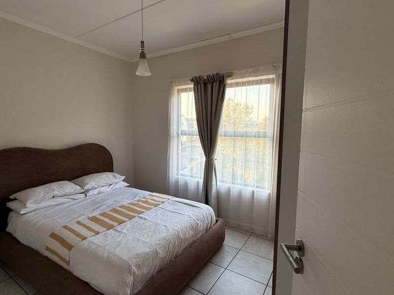 A well-lit bedroom featuring neutral wall tones, tiled flooring, and a large window with curtain tracks, offering a comfortable and functional living space.