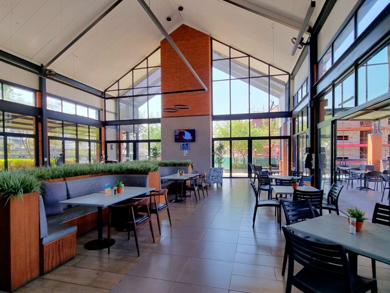 Spacious clubhouse area featuring a high vaulted ceiling, exposed brick architectural elements, and extensive floor-to-ceiling glass windows providing ample natural light.