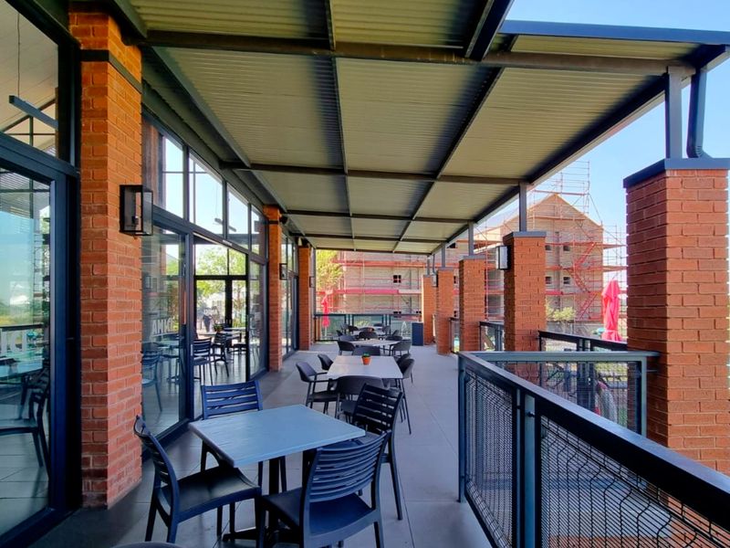 A spacious covered patio featuring brick pillars, metal roofing, and glass sliding doors, overlooking a swimming pool area.