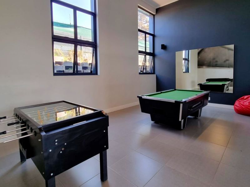 A spacious recreation room featuring large windows, neutral tiled flooring, and a large wall-mounted mirror, suitable for a games room or lounge area.