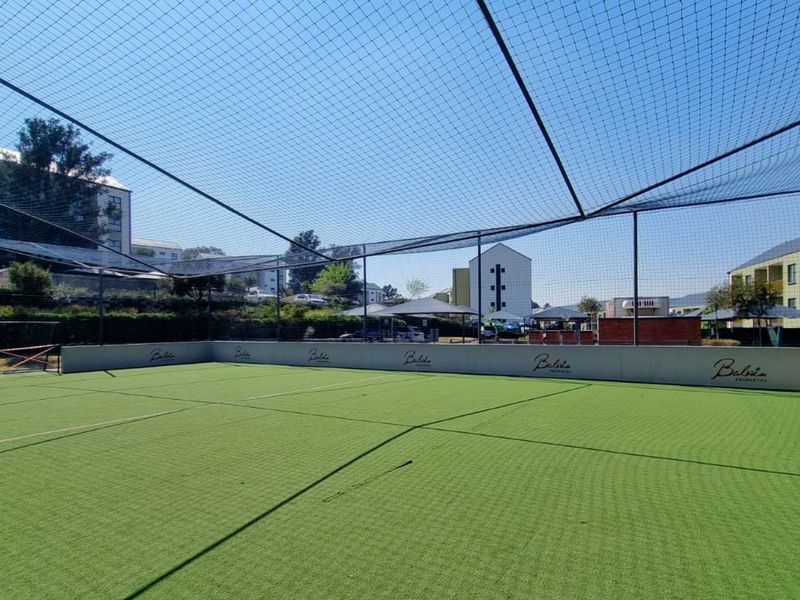 A well-maintained outdoor sports facility featuring artificial turf, enclosed by high perimeter netting and retaining walls, suitable for recreational activities.