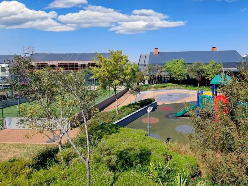 A well-maintained communal outdoor area featuring a playground, fenced sports court, and landscaped gardens within a residential apartment complex.