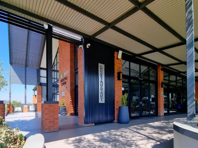Exterior view of a modern lifestyle centre clubhouse featuring exposed brickwork, metal roofing, and large glass entrance doors.