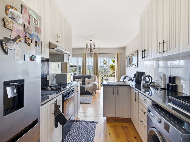 Open-plan kitchen featuring white cabinetry, granite countertops, and integrated appliances, flowing into a living area with access to a balcony.