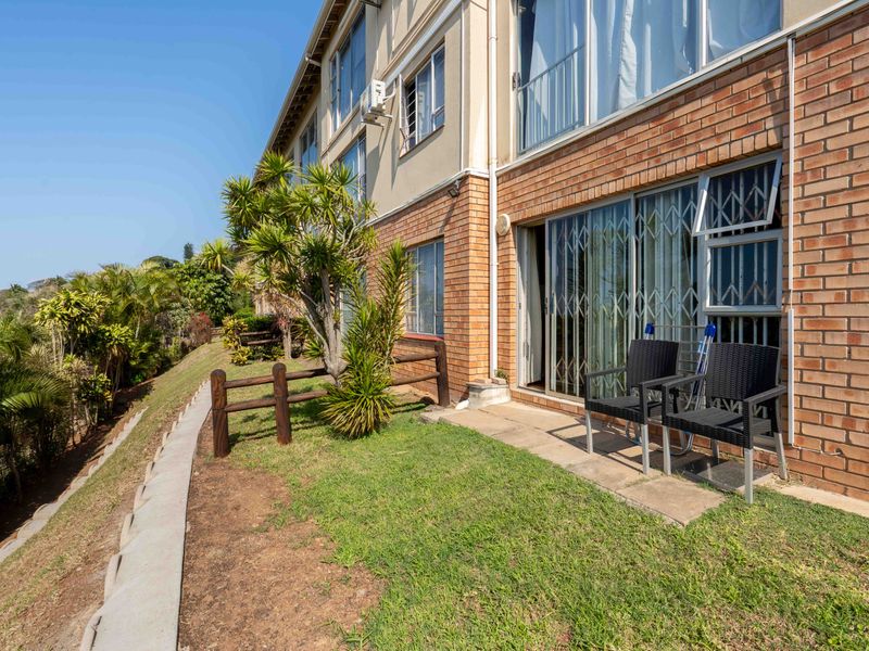 Rear exterior view of the flat featuring a brick facade, sliding glass doors with security gates, and a small garden area with a retaining wall.