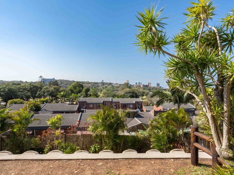 An elevated outdoor view overlooking the surrounding residential estate and landscape, featuring a concrete boundary wall and timber railing in the foreground.
