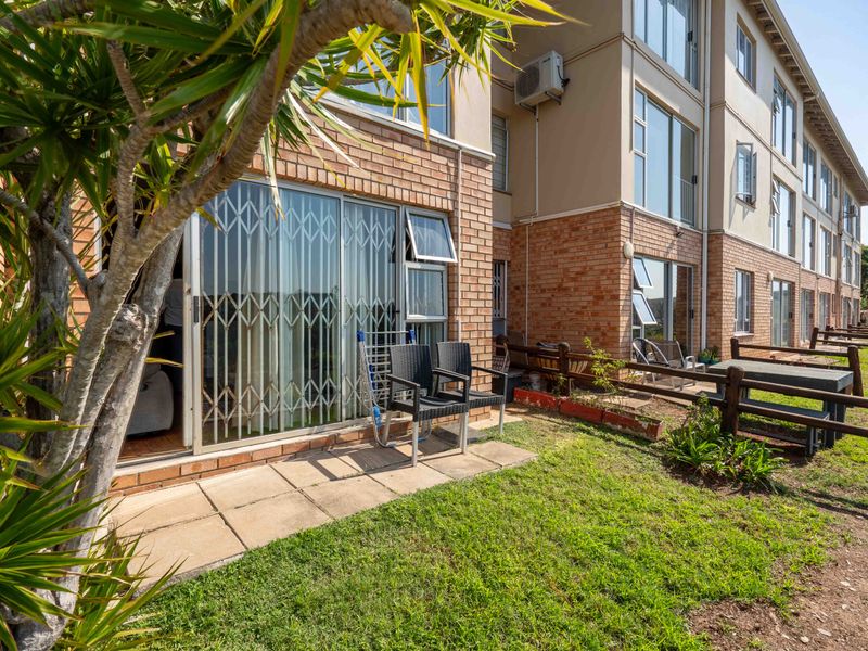 Rear view of the flat featuring a paved patio area, lawn, brick facade, and sliding glass doors with security gates.
