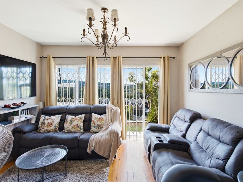 A well-maintained living room featuring hardwood flooring, a decorative chandelier, and a sliding glass door with security gate leading to an outdoor area.