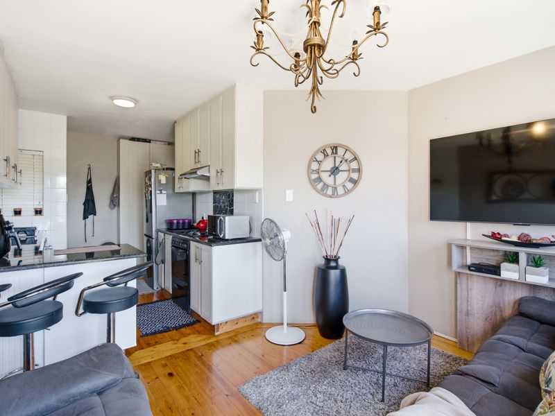Open-plan living area featuring a compact kitchen with granite countertops, breakfast bar, and warm hardwood flooring, seamlessly integrated with the lounge space.