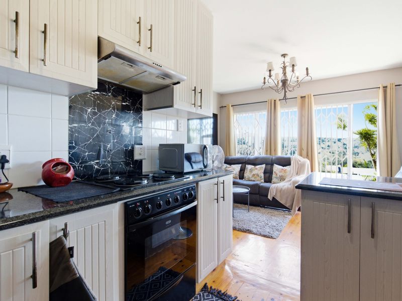 Open-plan kitchen featuring white cabinetry, granite countertops, and a marble-look splashback, flowing into a living area with wooden floors and natural light.