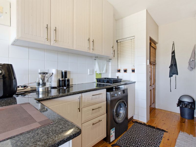 A functional kitchen featuring light-toned cabinetry, granite countertops, tiled backsplash, and integrated laundry facilities, complemented by warm timber flooring.