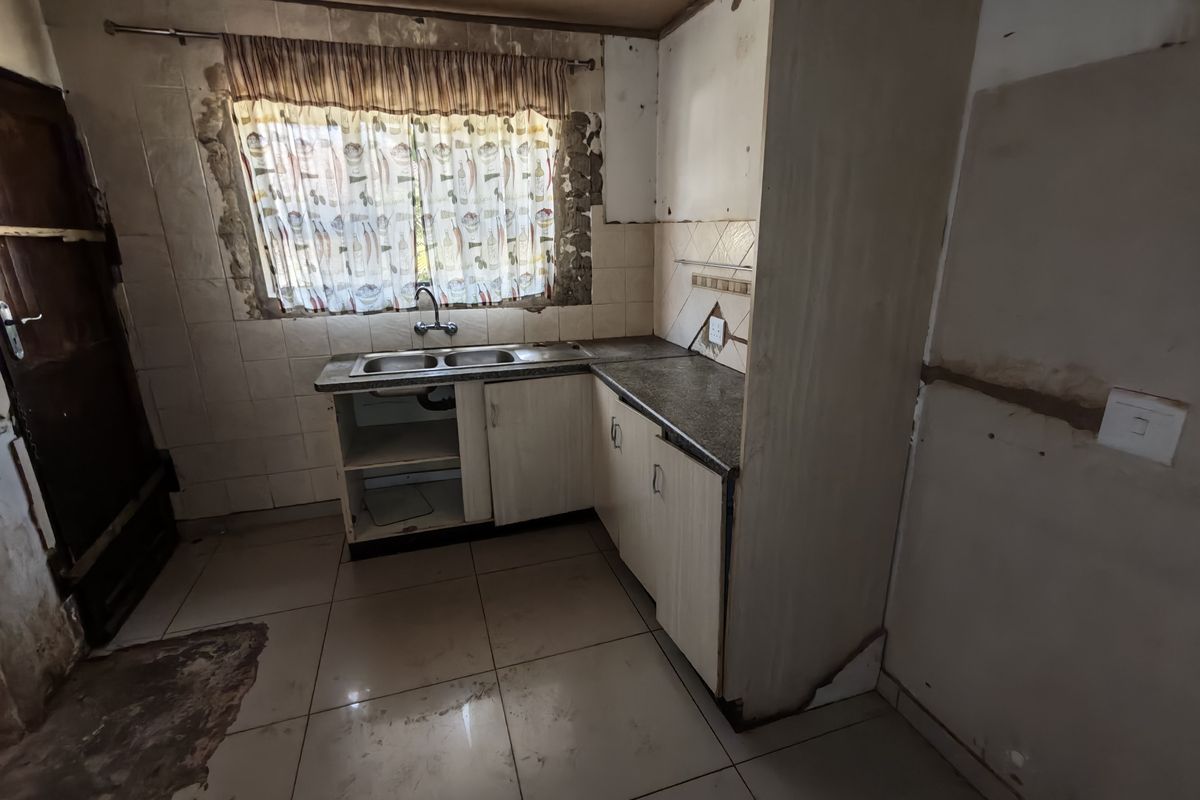 A dated kitchen space requiring significant renovation, featuring basic cabinetry, a double sink, and tiled finishes in need of repair.