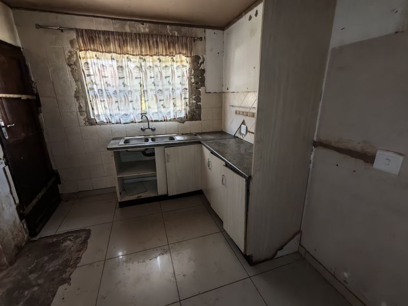 A dated kitchen space requiring significant renovation, featuring basic cabinetry, a double sink, and tiled finishes in need of repair.