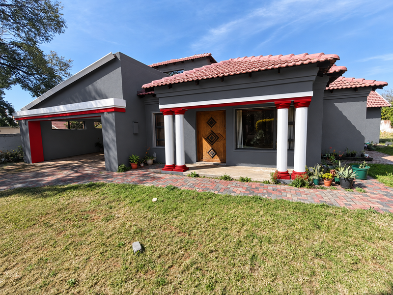 Front elevation of a modern house featuring a tiled roof, paved driveway, covered carport, and a distinctive entrance with decorative columns.