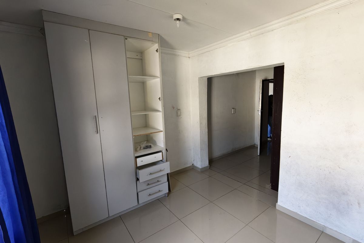 A vacant bedroom featuring tiled flooring, a built-in wardrobe, and coved ceiling cornices, requiring cosmetic updates to the wall finishes.