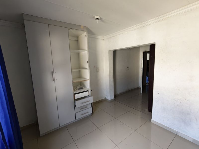 A vacant bedroom featuring tiled flooring, a built-in wardrobe, and coved ceiling cornices, requiring cosmetic updates to the wall finishes.