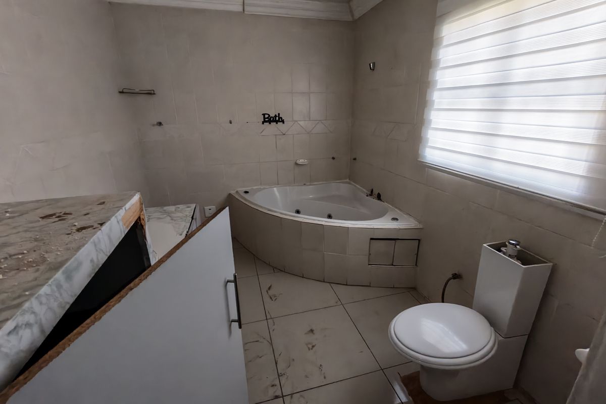 A dated bathroom featuring a corner spa bath, toilet, and tiled finishes, currently requiring maintenance and cosmetic updates to restore its functionality and appeal.
