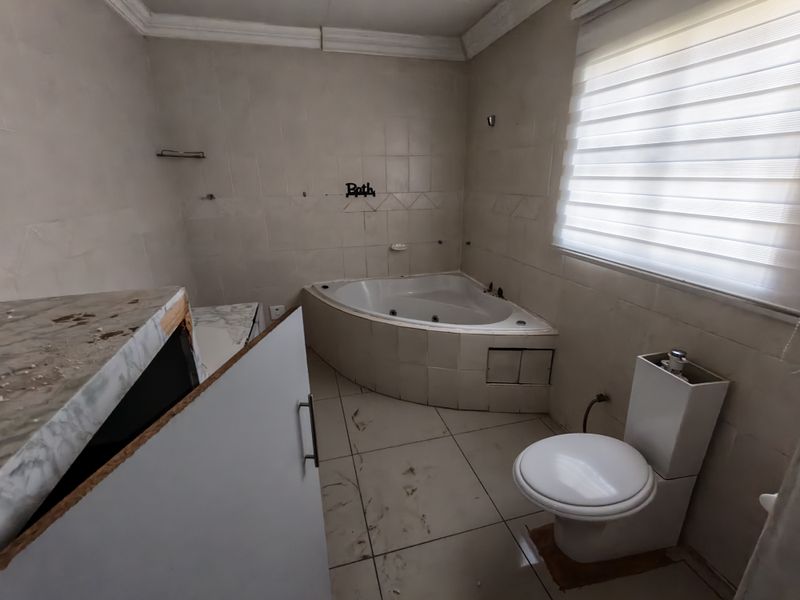 A dated bathroom featuring a corner spa bath, toilet, and tiled finishes, currently requiring maintenance and cosmetic updates to restore its functionality and appeal.