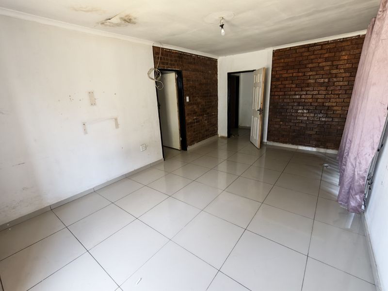 An empty living area featuring ceramic floor tiles and an exposed brick feature wall, requiring maintenance to the ceiling and wall finishes.