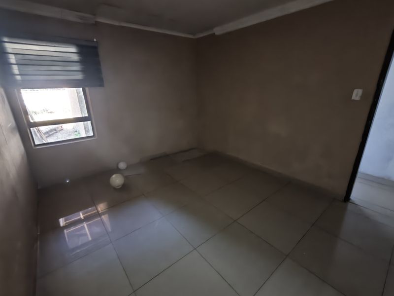 An empty bedroom featuring tiled flooring and a window with a roller blind, currently requiring wall finishing and painting.