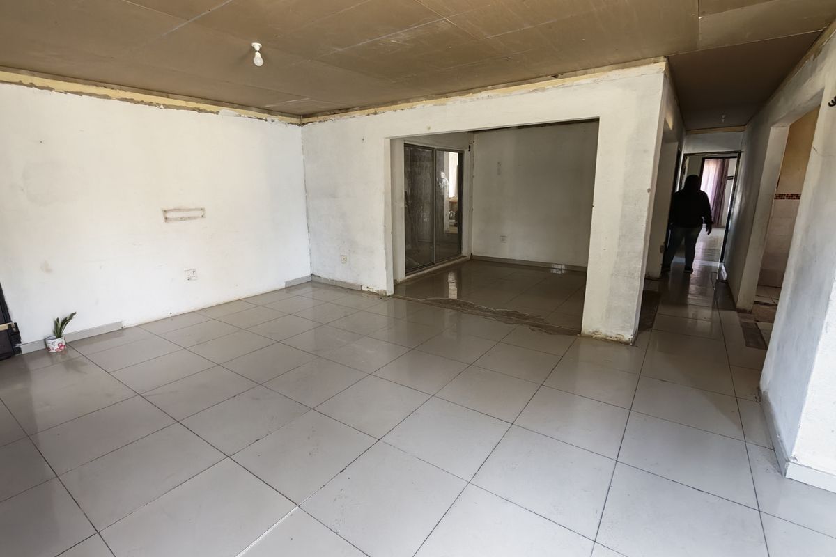 An empty, unfinished living area featuring ceramic floor tiles, a sliding glass door, and exposed ceiling panels, requiring renovation and finishing touches.
