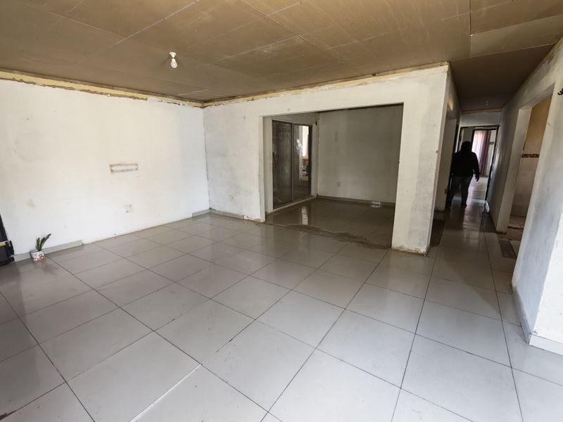 An empty, unfinished living area featuring ceramic floor tiles, a sliding glass door, and exposed ceiling panels, requiring renovation and finishing touches.