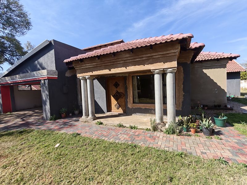 Front elevation of a house featuring a covered entrance porch with concrete columns, tiled roof, and a paved driveway area requiring exterior maintenance.