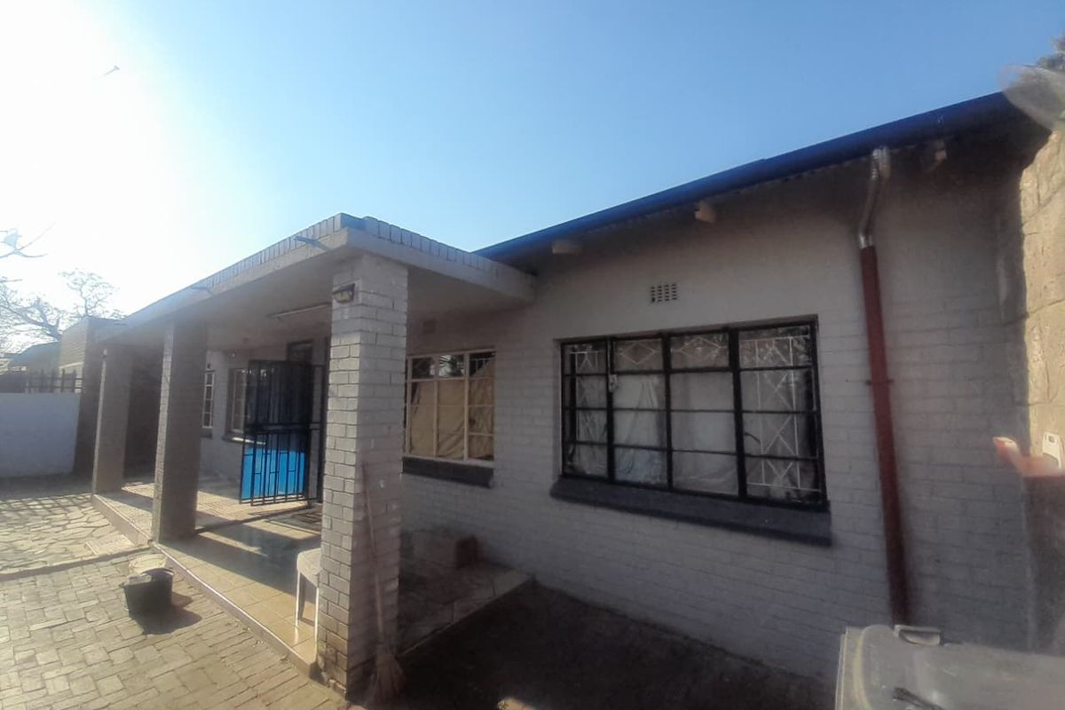 Rear view of the property featuring a covered patio area, brick facade, and paved outdoor space with security bars on the windows.