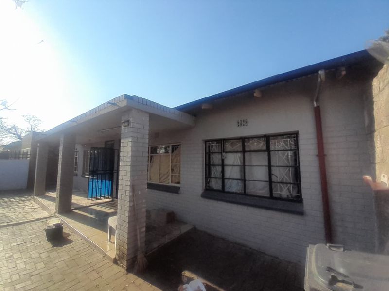 Rear view of the property featuring a covered patio area, brick facade, and paved outdoor space with security bars on the windows.