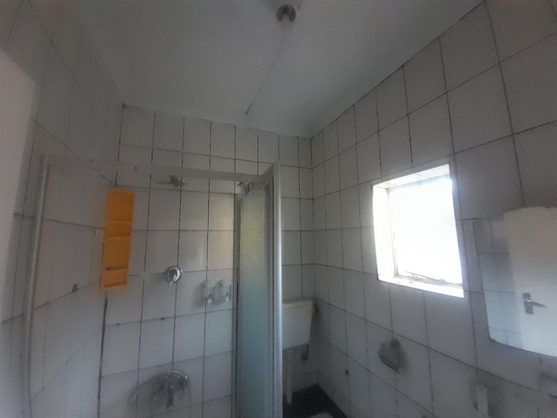 A dated bathroom featuring a shower enclosure, tiled walls, and a toilet, requiring renovation to update the finishes and fixtures.