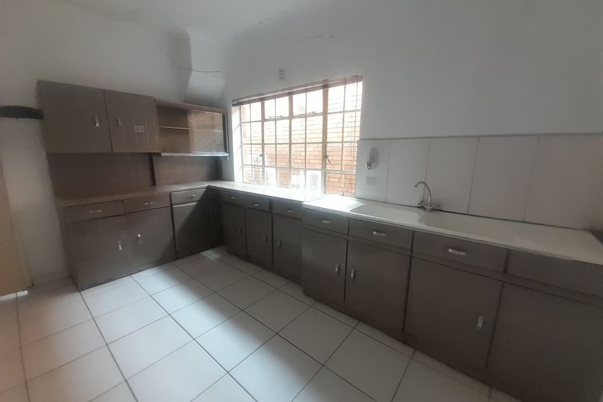 A dated, empty kitchen featuring original built-in cabinetry, tiled flooring, and a functional sink area, offering significant potential for a modern renovation.