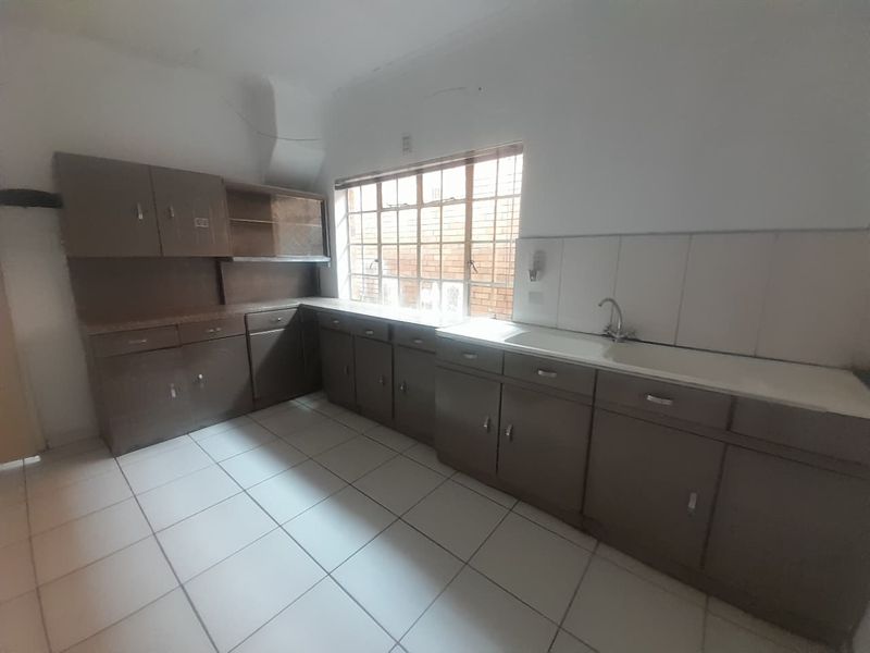 A dated, empty kitchen featuring original built-in cabinetry, tiled flooring, and a functional sink area, offering significant potential for a modern renovation.