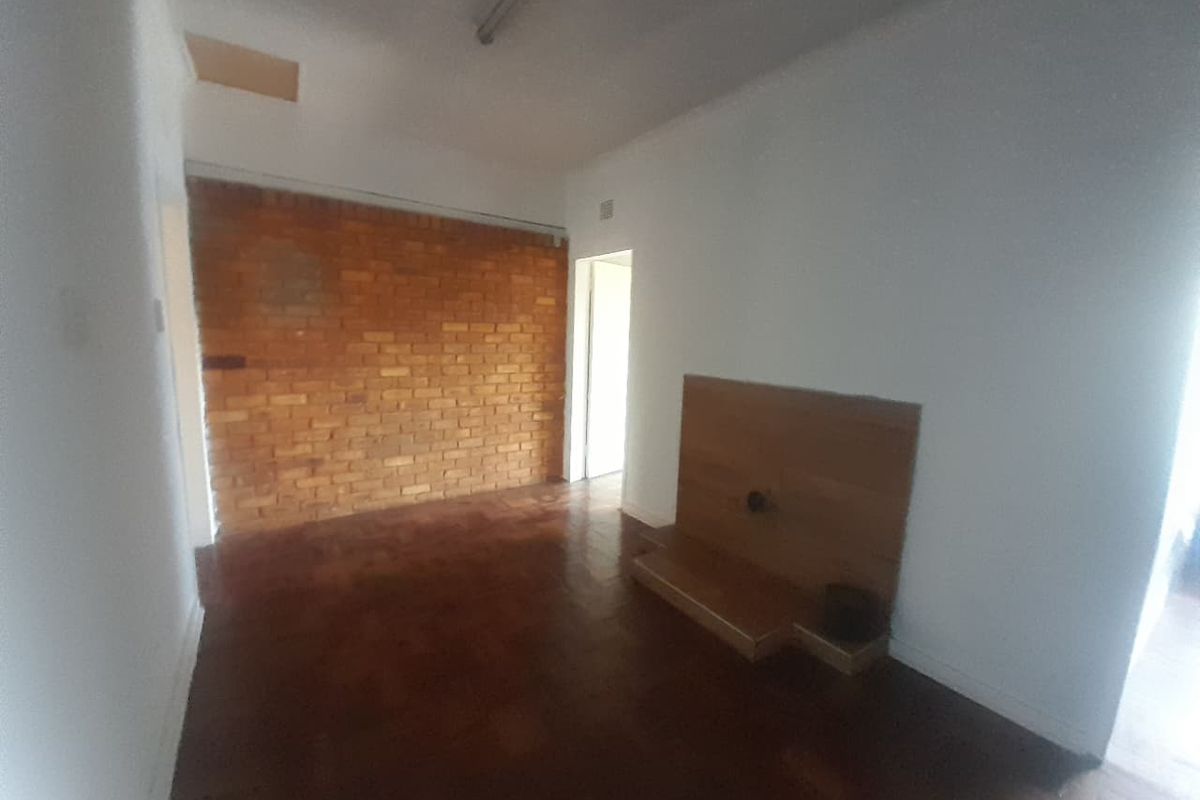 An empty living room featuring a characterful exposed brick wall, traditional parquet flooring, and a built-in wooden media console.