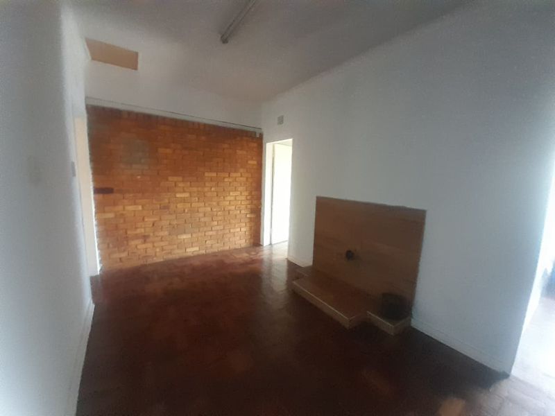 An empty living room featuring a characterful exposed brick wall, traditional parquet flooring, and a built-in wooden media console.