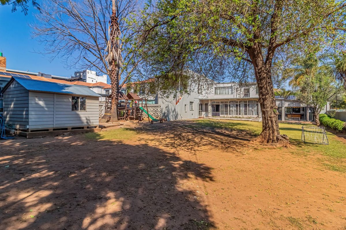 Spacious rear garden featuring a large lawn, mature trees, and a detached storage shed, providing ample outdoor space.