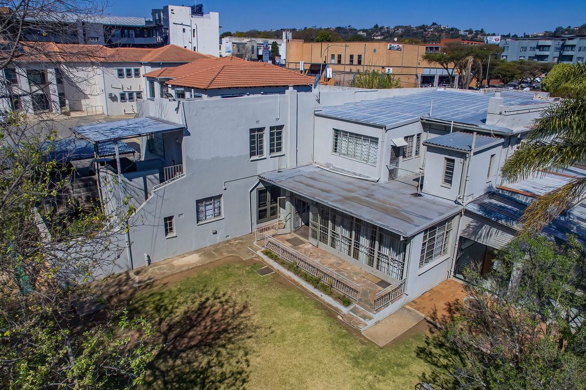 Aerial view of the property showing the rear garden, stone patio, and multi-level building structure with a mix of tiled and metal roofing.