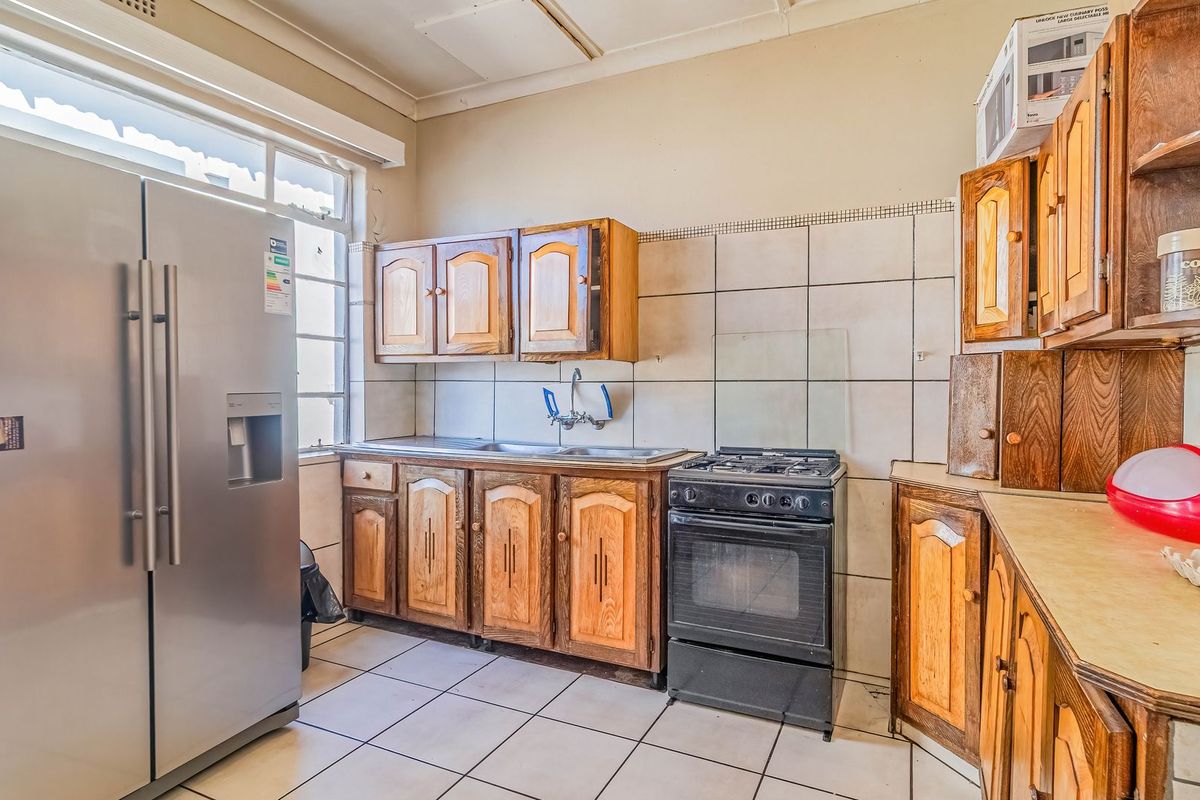 A functional kitchen featuring wooden cabinetry, tiled splashbacks, tiled flooring, and a freestanding gas stove, offering potential for a modern renovation.