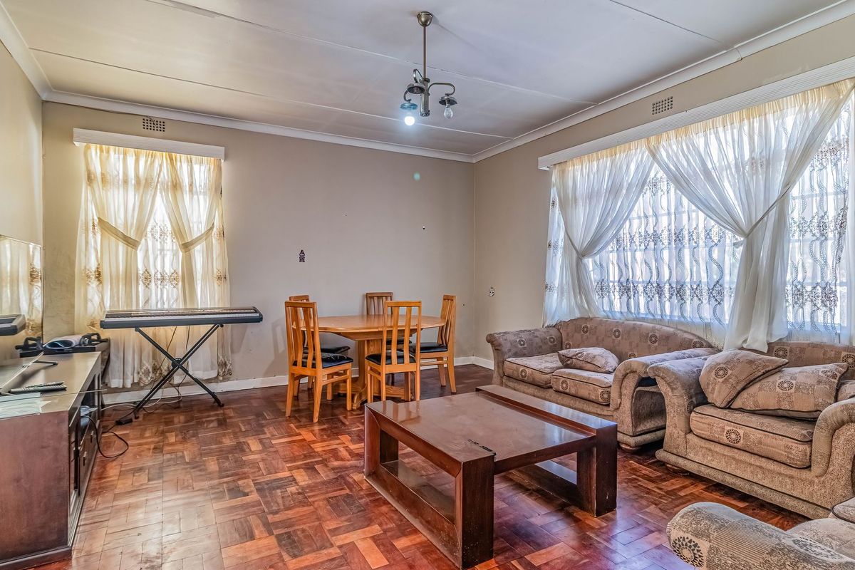 Spacious living room featuring classic parquet flooring, neutral wall tones, and large windows with natural light, offering a versatile layout for comfortable family living.