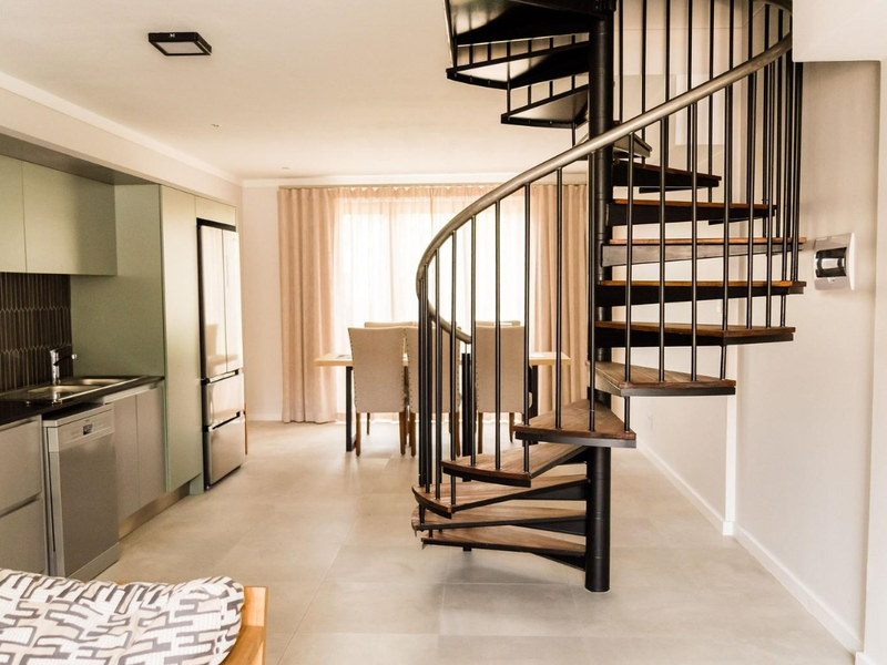 Modern open-plan living area featuring a striking spiral staircase, contemporary kitchen cabinetry, integrated appliances, and neutral tiled flooring throughout.