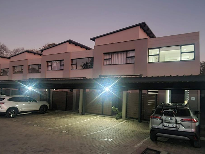 Front elevation of a modern townhouse complex featuring covered carports, paved parking areas, and contemporary architectural design with aluminium window frames.