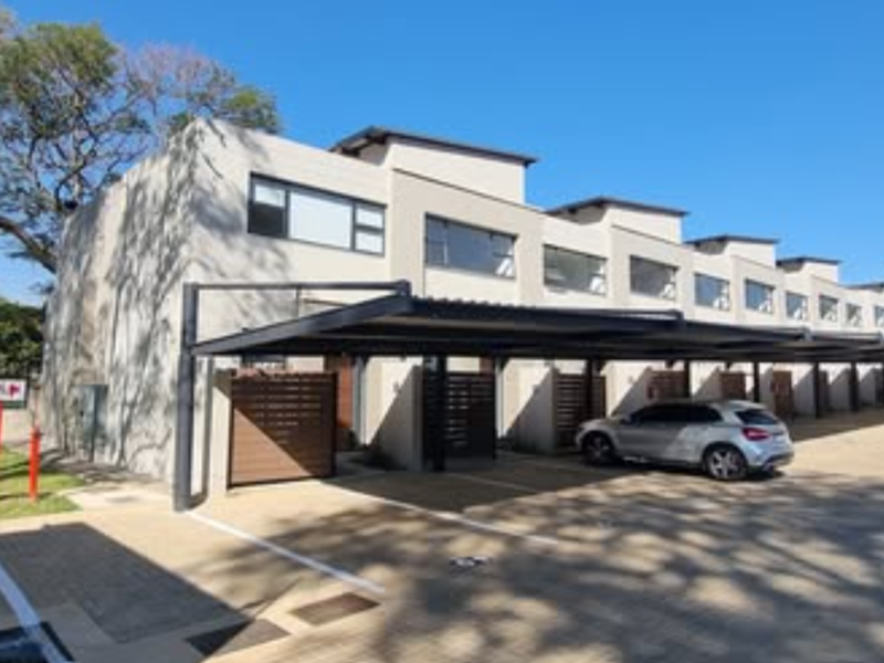 Modern townhouse complex exterior featuring a row of covered parking bays, paved driveway, and contemporary architectural design with timber privacy screens.