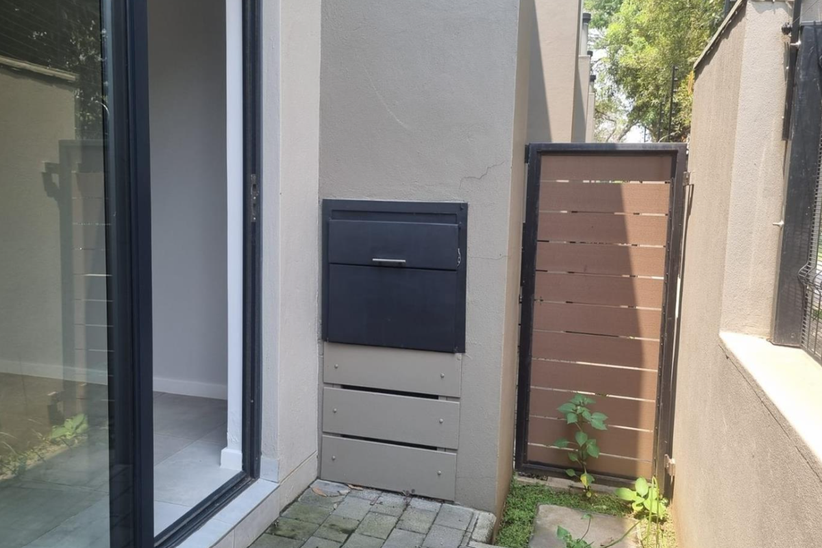 A side exterior view of the townhouse featuring a sliding glass door, a built-in wall safe, and a pedestrian gate with paved access.