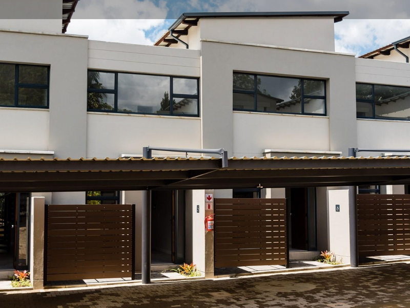 Modern townhouse exterior featuring a covered carport, paved driveway, and private timber screening for each unit entrance.