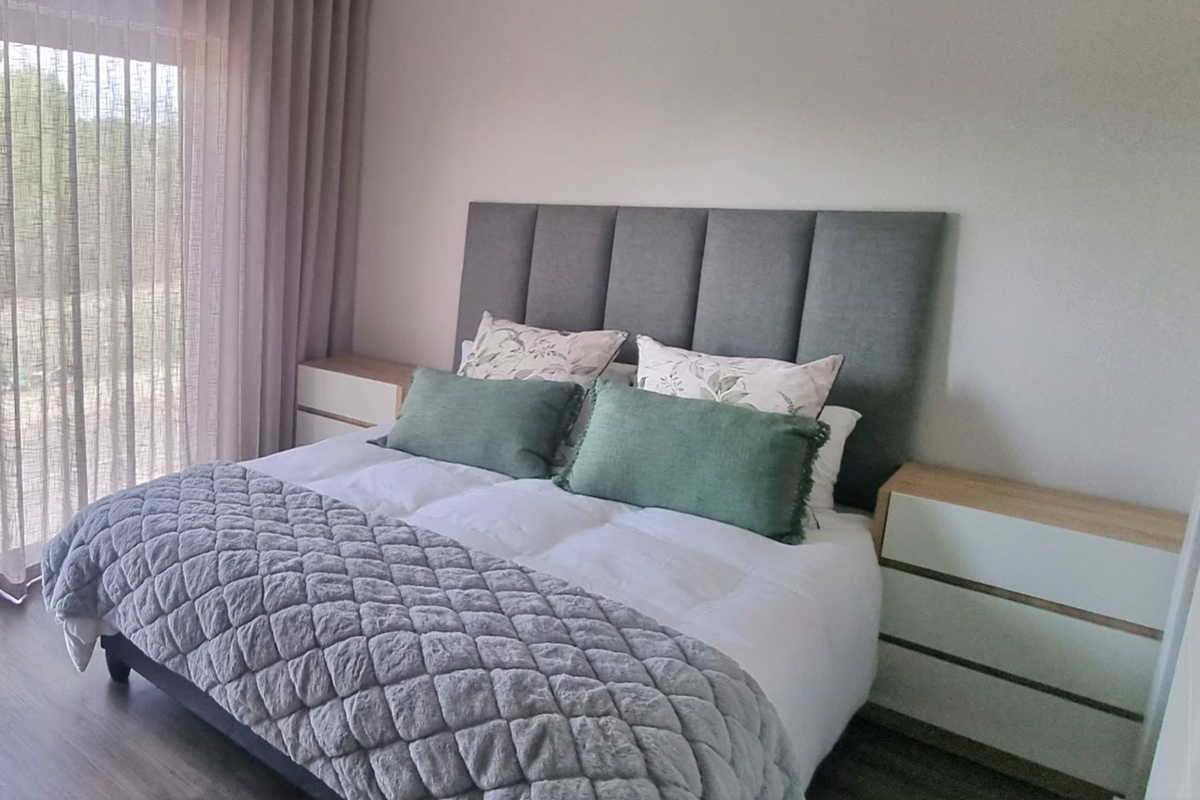 A well-maintained bedroom featuring a modern upholstered headboard, laminate flooring, and large sliding glass doors providing natural light.
