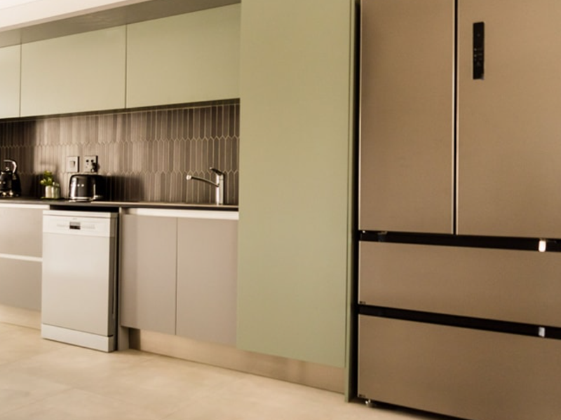 Modern kitchen featuring sage green cabinetry, sleek tiled backsplash, integrated oven, and high-quality tiled flooring in a contemporary townhouse setting.