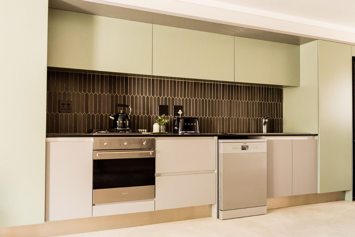 Modern kitchen featuring sage green cabinetry, dark vertical tiled backsplash, integrated appliances, and sleek stone countertops.