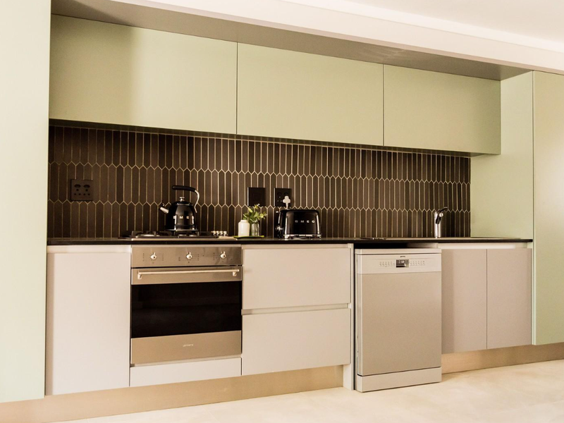 Modern kitchen featuring sage green cabinetry, dark vertical tiled backsplash, integrated appliances, and sleek stone countertops.