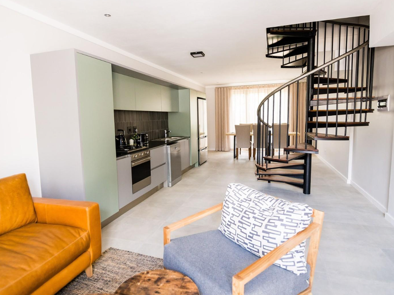 Modern open-plan living area featuring a sleek kitchen with built-in appliances and a striking spiral staircase leading to the upper level.