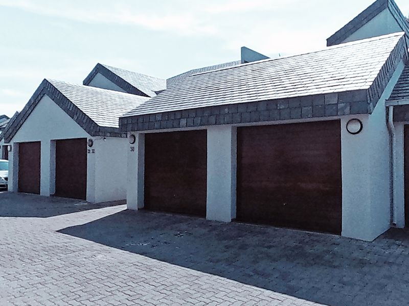 A view of the townhouse complex featuring multiple garage units with dark wood-finish doors and paved driveway access.