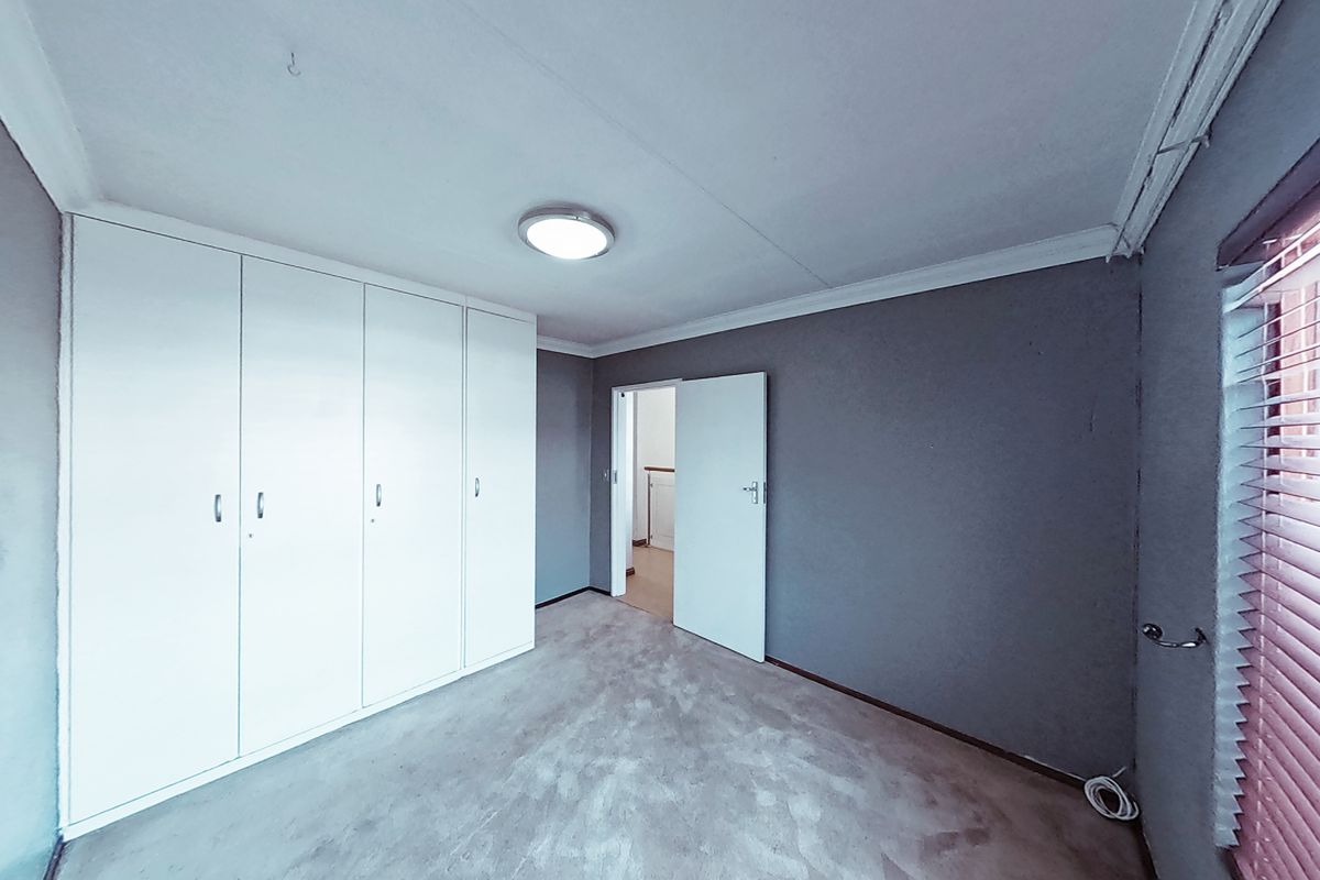 An empty bedroom featuring built-in cupboards, grey walls, and venetian blinds, offering a blank canvas for personalization.